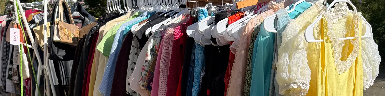A Locket Vintage clothing rack at an outdoor Charlotte market, packed with colourful vintage dresses and tops on hangers.